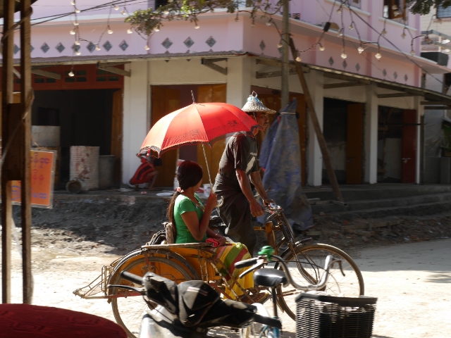 Dreirädriges Fahrrad, Mann fährt, Frau mit Sonnenschirm auf dem Beifahrersitz