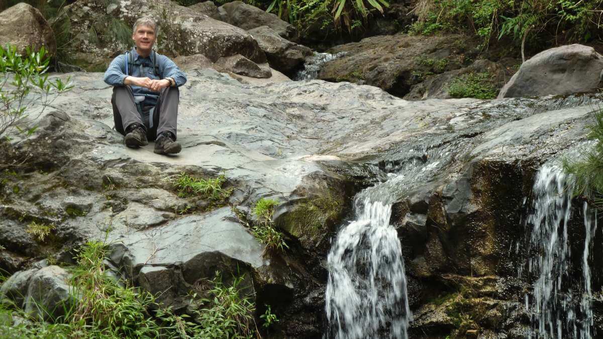 Marcus sitzt auf einem Felsplateau neben einem kleinen Wasserfall.