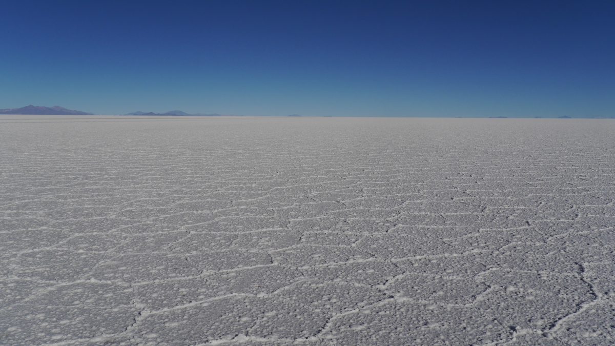 Eine weite Fläche der Uyuni-Salzebene unter einem klaren blauen Himmel, gekennzeichnet durch ein geometrisches Muster aus flachen, weißen Salzkrusten.