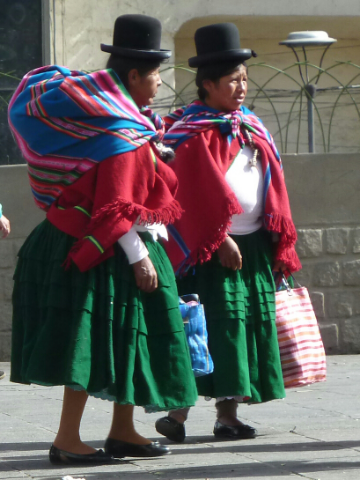Zwei indigene Frauen mit grünen Röcken und roten Jacken.