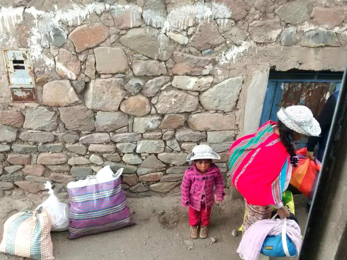 Indigene Frau mit kleinem Kind und vielen Taschen steht neben dem Bus zum Colca Canyon.