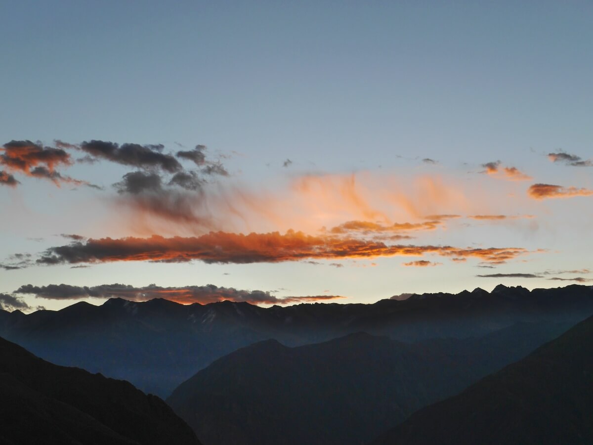 Rötliche Wolken am Himmel über schwarzen Bergen.