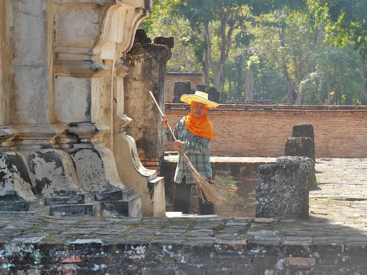 Person mit Sonnenhut und Reisigbesen vor dem Tempel.