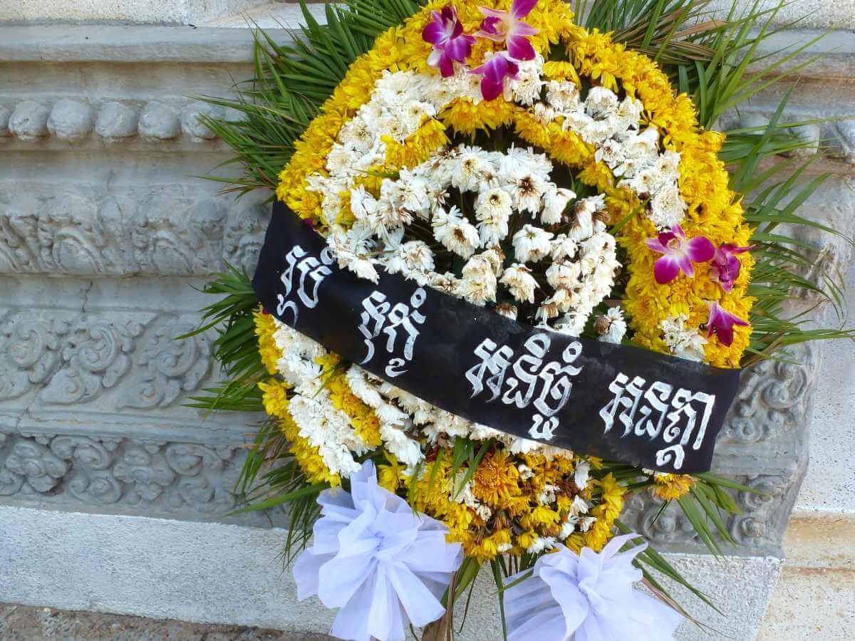 Kranz aus gelben und weißen Blüten vor dem Stupa der Killing Fields.