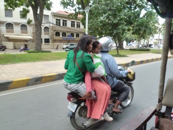 Drei Personen auf einem Motorroller. Einer jungen Frau fehlt ein Teil ihres Beins