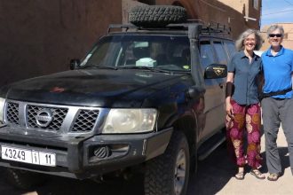 Gina und Marcus neben einem großen schwarzen Geländewagen