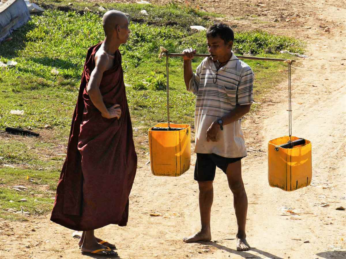 Buddhistischer Mönch unterhält sich mit einem Wasserträger.