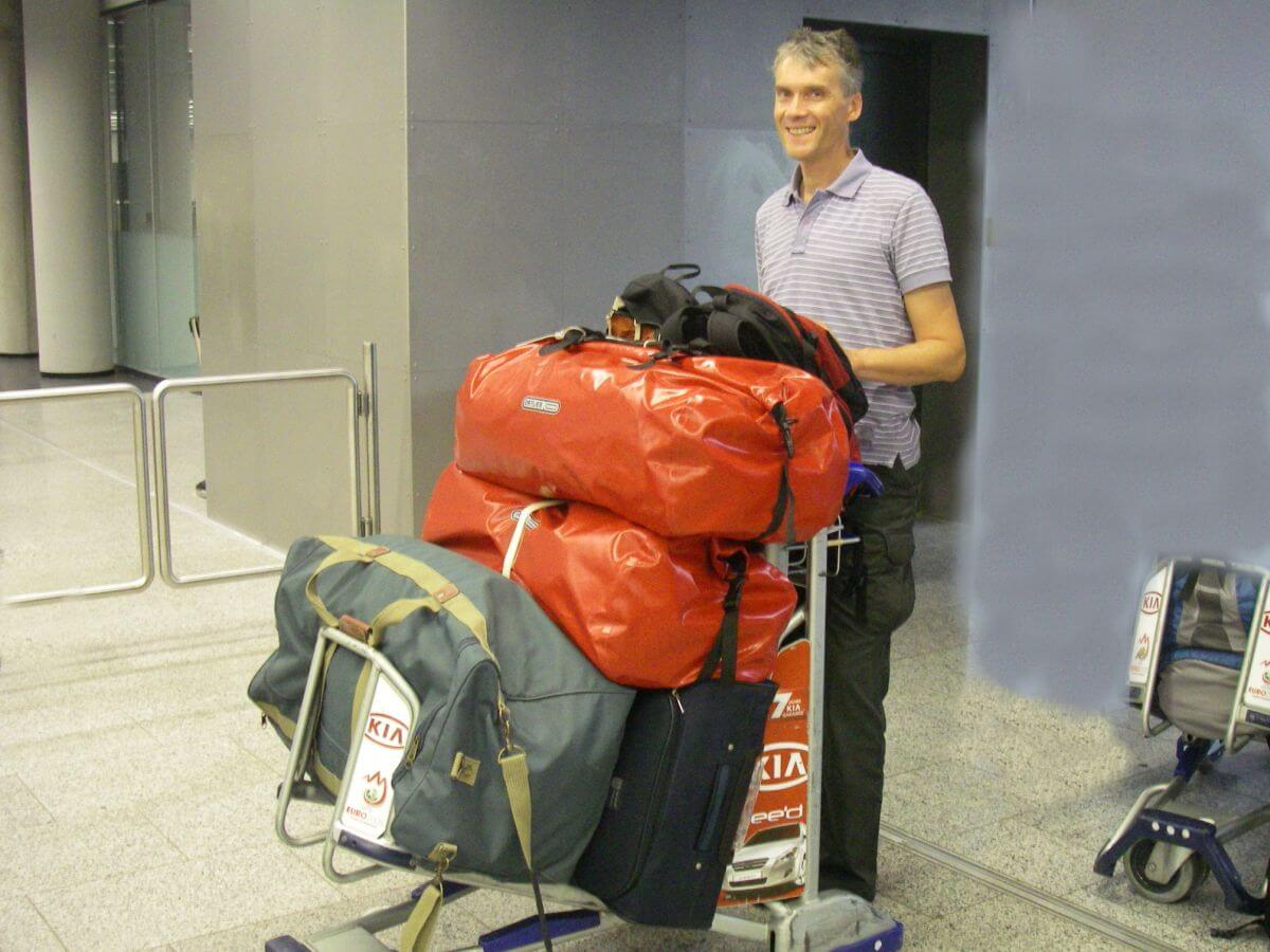 Marcus schiebt einen Gepäckwagen mit vier großen Reisetaschen.