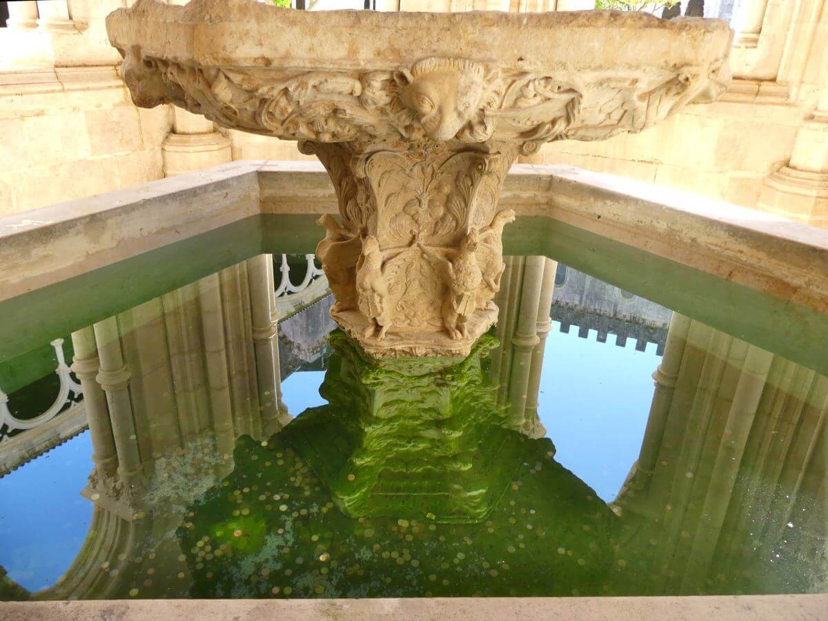 Brunnen, im Wasser spiegelt sich die Fassade des Kreuzgangs.