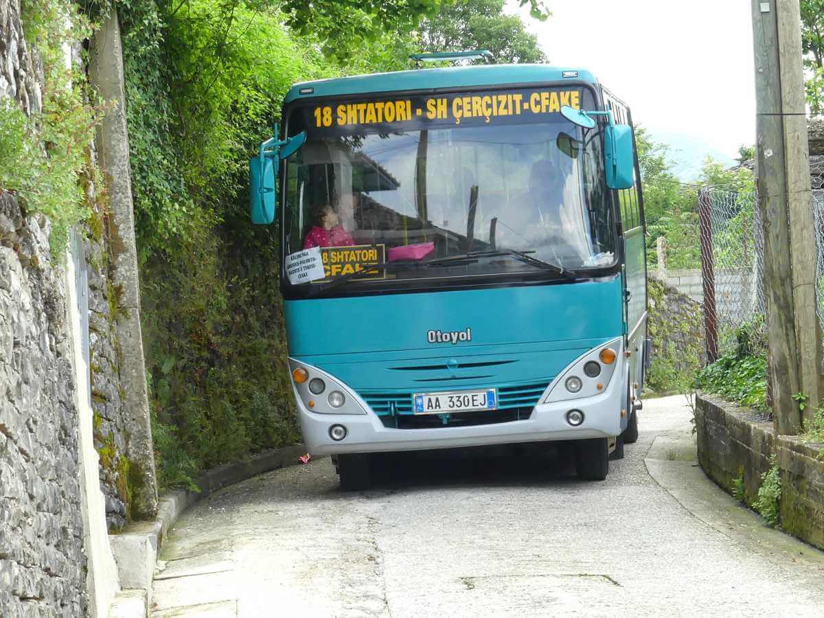 Blauer Minibus auf einer engen Straße mit Mauern rechts und links.