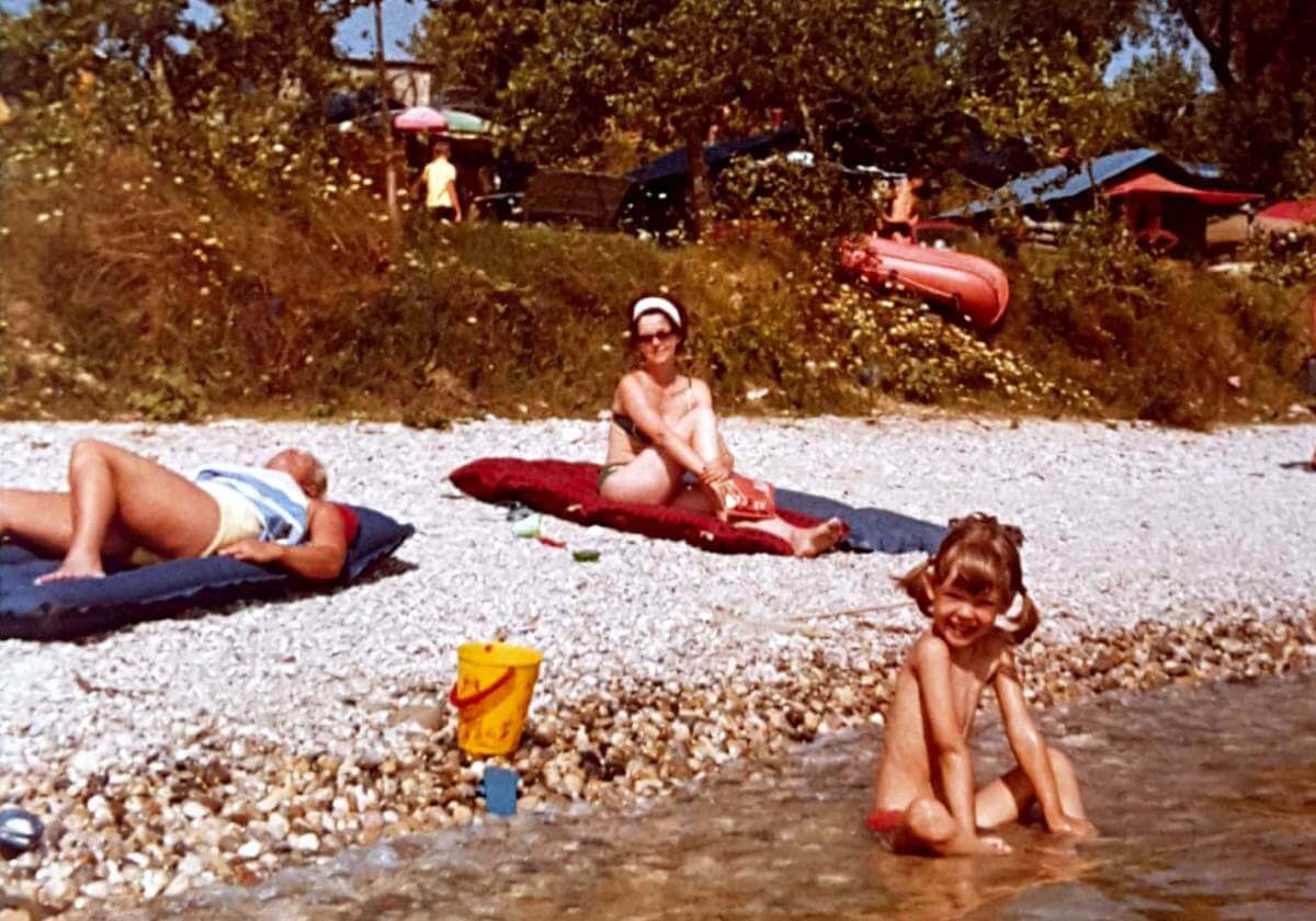 Mädchen sitzt im flachen Wasser am Kiesstrand.