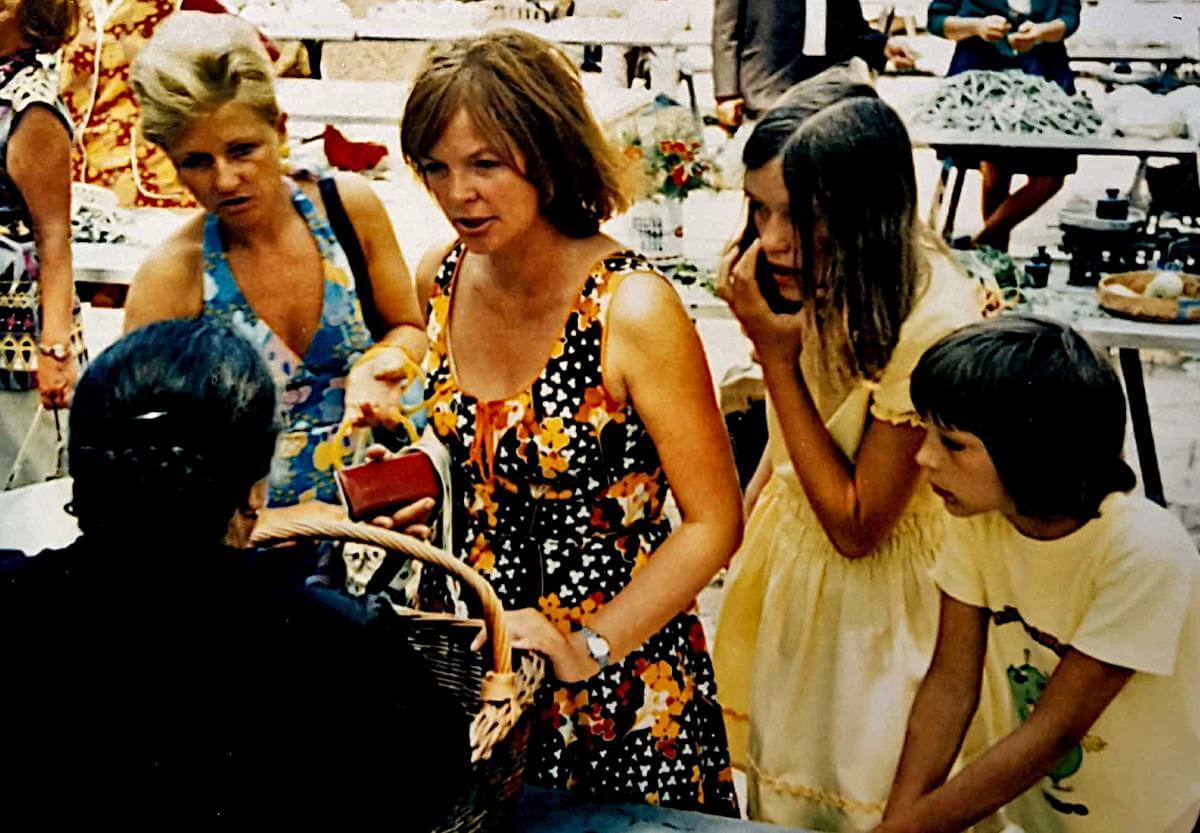 Zwei Frauen und zwei Kinder am Marktstand mit einer älteren Verkäuferin.