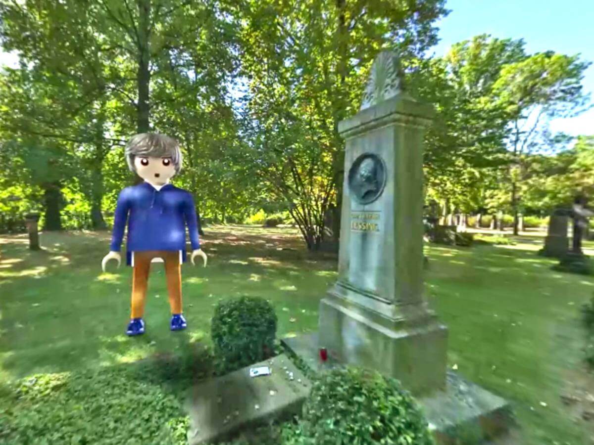 Playmobilfigur auf grünem Friedhof neben Grab.