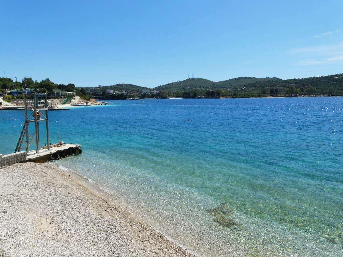 Strand mit kleinem Steg und blauem Meer.