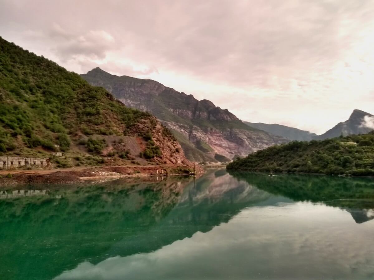 Berge und Wolken spiegeln sich in grünem See.