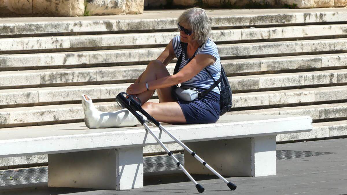 Frau mit Gipsbein und Krücken sitzt auf einer Bank.