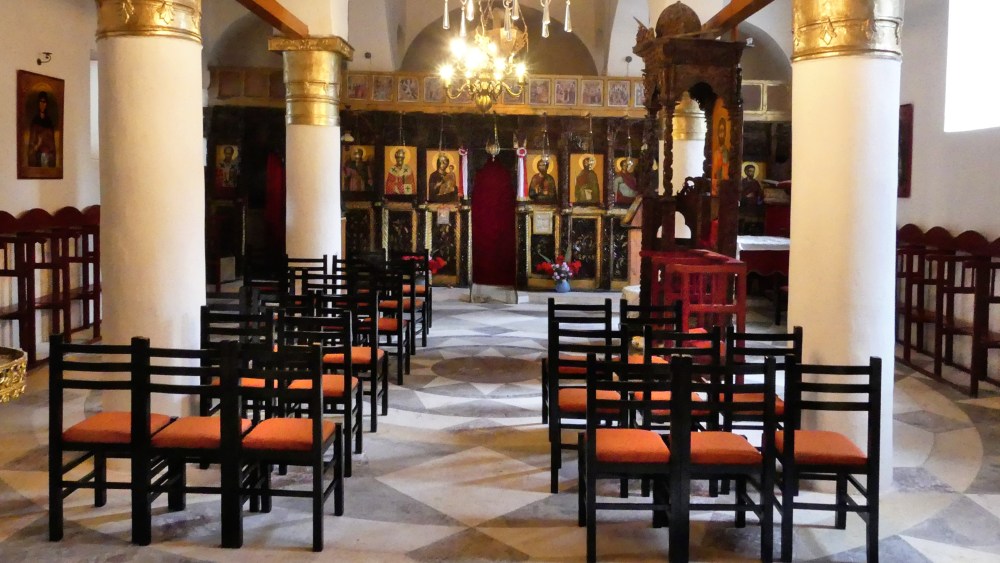 Innenraum der Kirche mit weißen Säulen und dunklem Holzschnitzwerk.