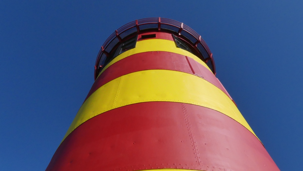 rot-gelb geringelter Leuchtturm vor blauem Himmel.