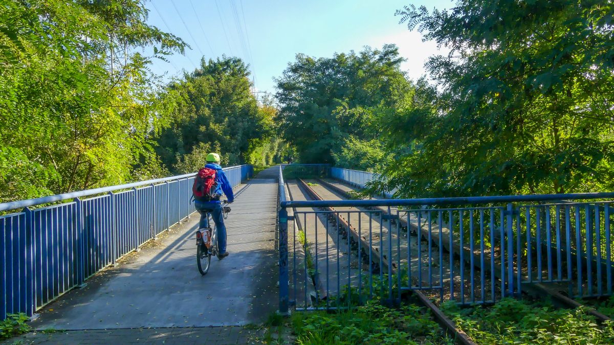 Radler überquert eine Brücke der Erzbahntrasse, auf der noch alte Schienen zu sehen sind.