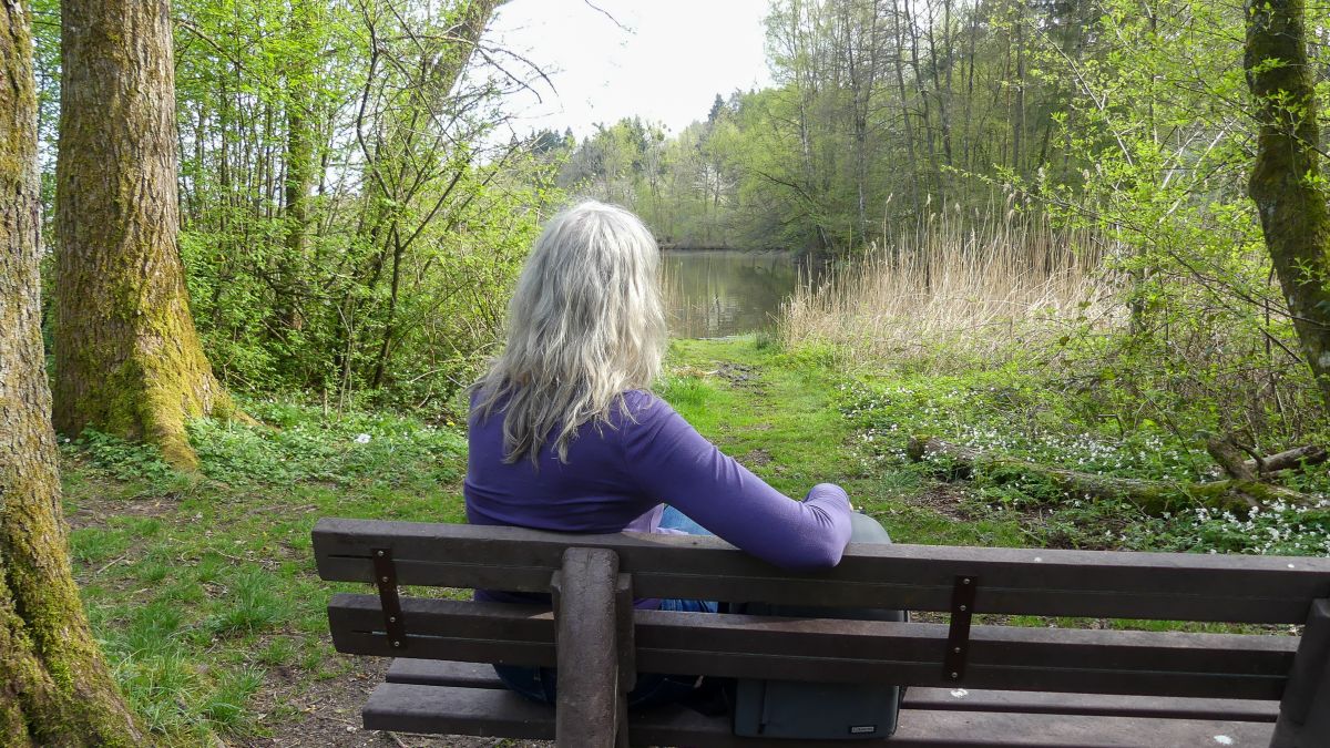 Gina sitzt auf einer Bank am See.