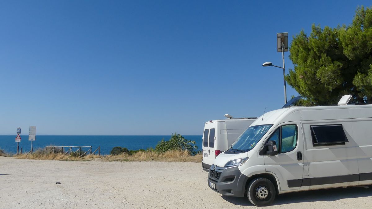 Wohnmobiltour Italien: Zwei Campervan stehen auf einem Parkplatz am Meer.