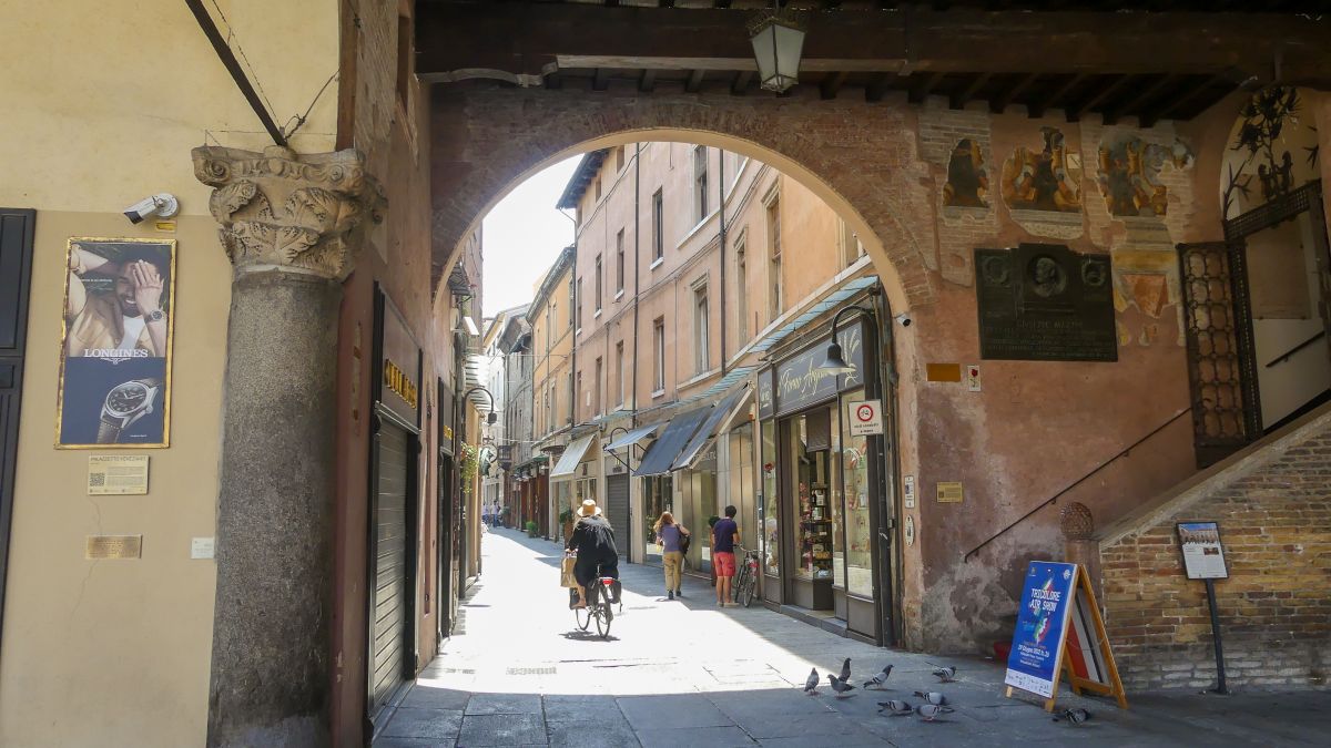 Eine Frau fährt mit einem Fahrrad durch einen Torbogen in der Altstadt von Ravenna.