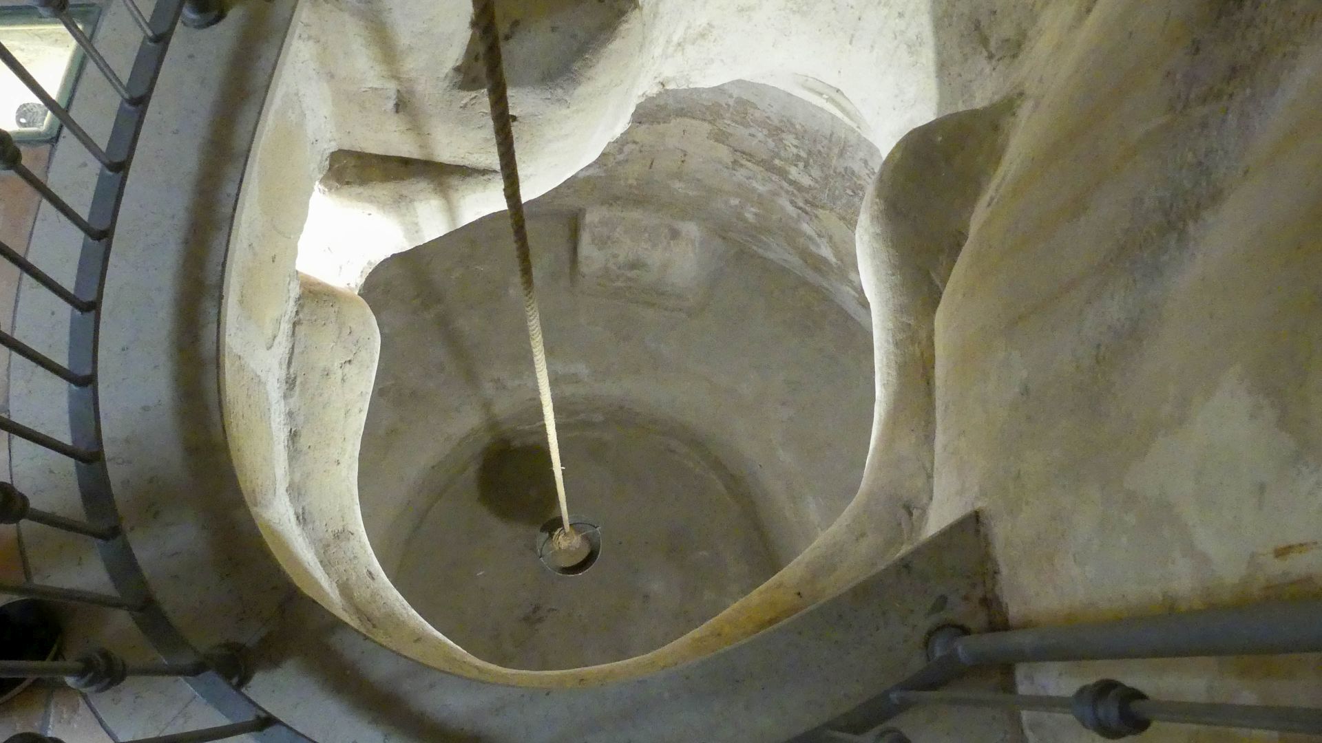 Blick von oben in den Brunnenschacht der Zisterne, ein Eimer hängt an einem langen Seil.