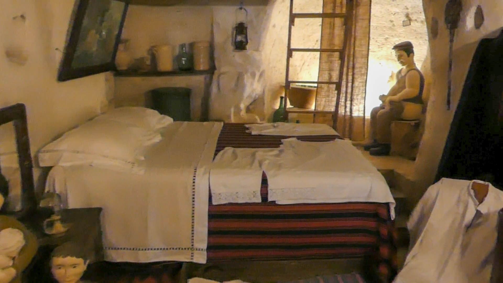 Schlafnische in der Höhlenwohnung mit Doppelbett und Figur auf Toiletteneimer.