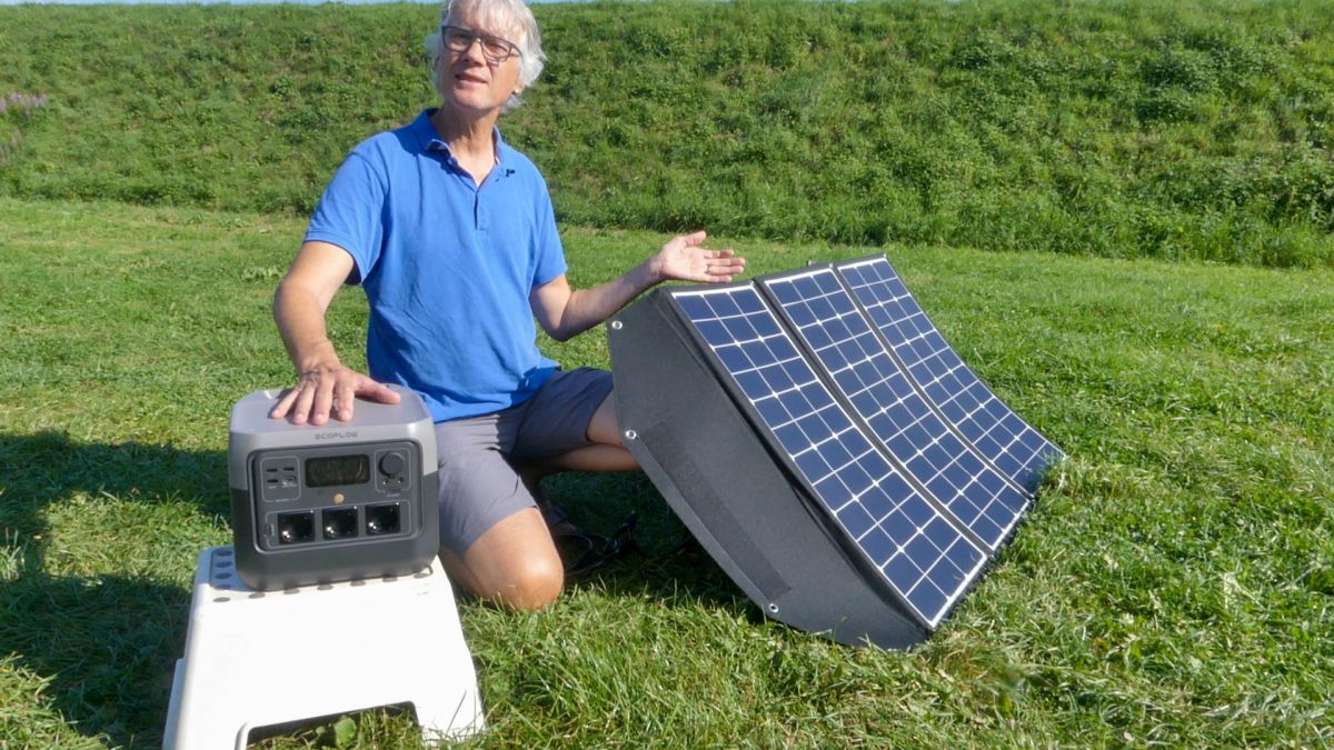 Marcus kniet auf dem Rasen, mit der Ecoflow Powerstation und dem Sunfolder vor sich.