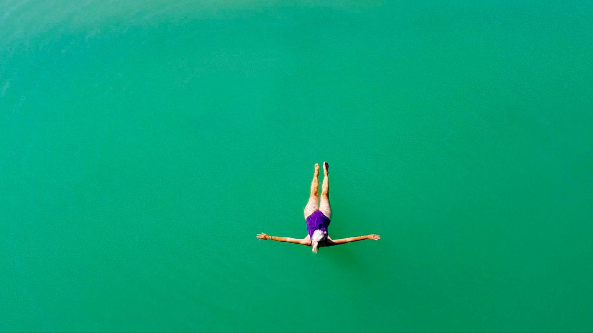 Luftbild auf Schwimmerin in smaragdgrünem Wasser.