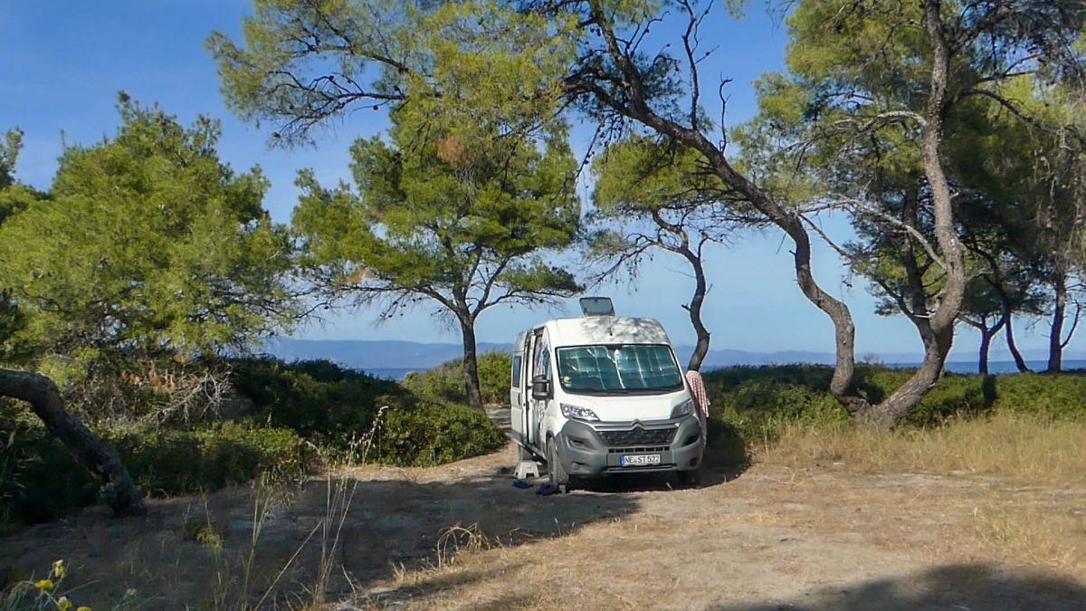 Weißer Van steht unter Pinien am Strand in Griechenland.