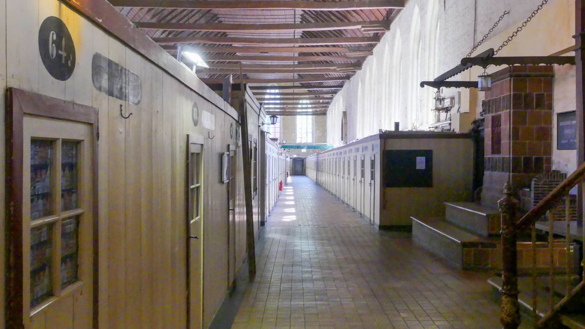 Lange Halle mit Bretterbuden zu beiden Seiten.