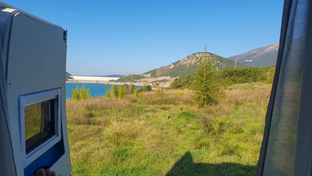 Blick aus geöffneten Hecktüren des Wohnmobils auf einen türkisblauen See und grüne Landschaft.