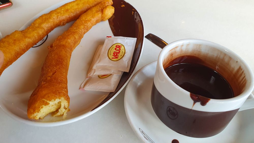 Teller mit Churros, daneben eine Tasse mit dickflüssiger heißer Schokolade.