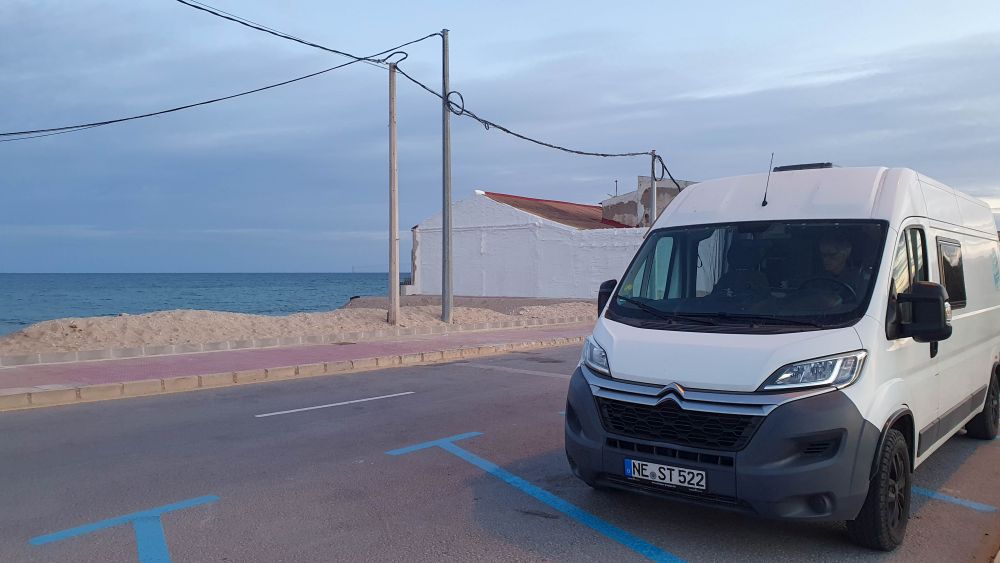 Wohnmobil steht auf mit blauen Linien markiertem Parkplatz am Meer.