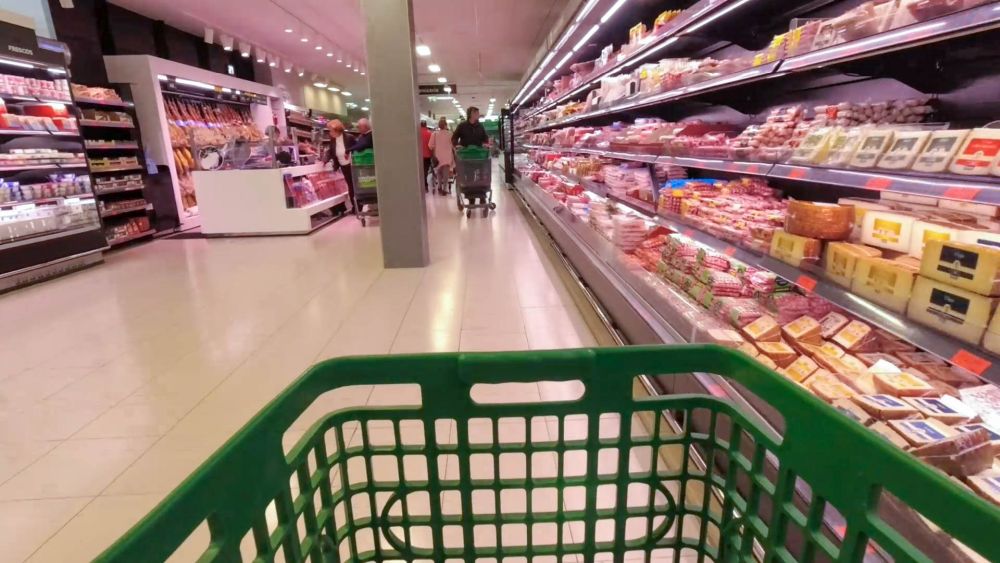 Blick über den Einkaufswagen in die Reihe mit Kühlregalen im Supermarkt.