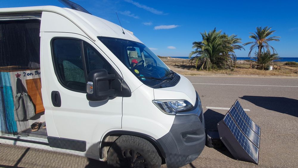 Vor dem Wohnmobil steht ein faltbares Solarmodul zur Stromversorgung.