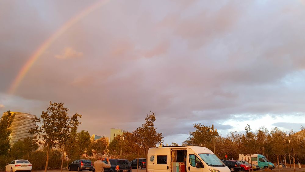 Wohnmobil steht auf einem großen Parkplatz, am Himmel ein Regenbogen.