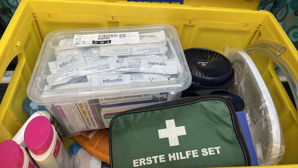 Ein gelber Kasten mit einem grünen Erste-Hilfe-Kasten, medizinischem Material, Verbandszeug, einem tragbaren Ventilator und Toilettenartikeln.