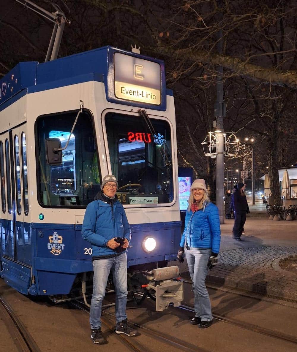 Zwei Personen in blauen Jacken und Wintermützen stehen vor einer blauen Straßenbahn mit der Aufschrift 