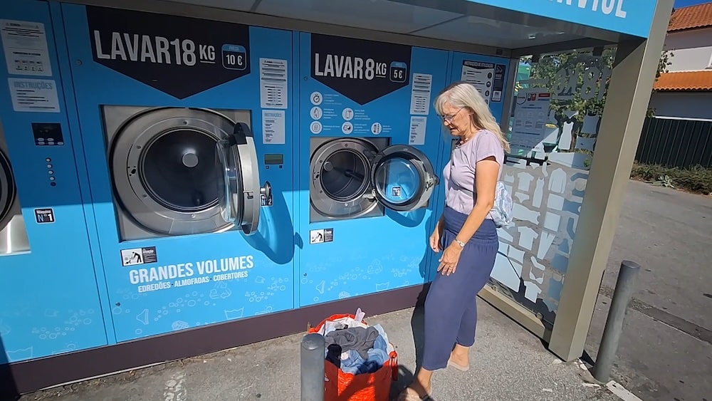 Eine Frau steht vor einer Selbstbedienungs-Waschmaschine im Freien und bereitet sich darauf vor, Wäsche aus einer roten Tasche zu waschen.