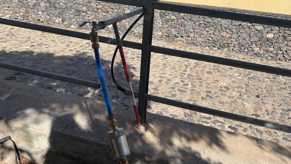 Einfache Wasserleitung aus Metallrohr, an einem Geländer befestigt.