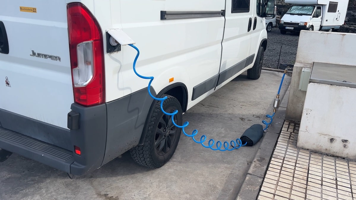 Ein weißer Van steht neben der Wasserzapfstelle, ein blauer Schlauch mit Wasserfilter führt zum Tankstutzen.