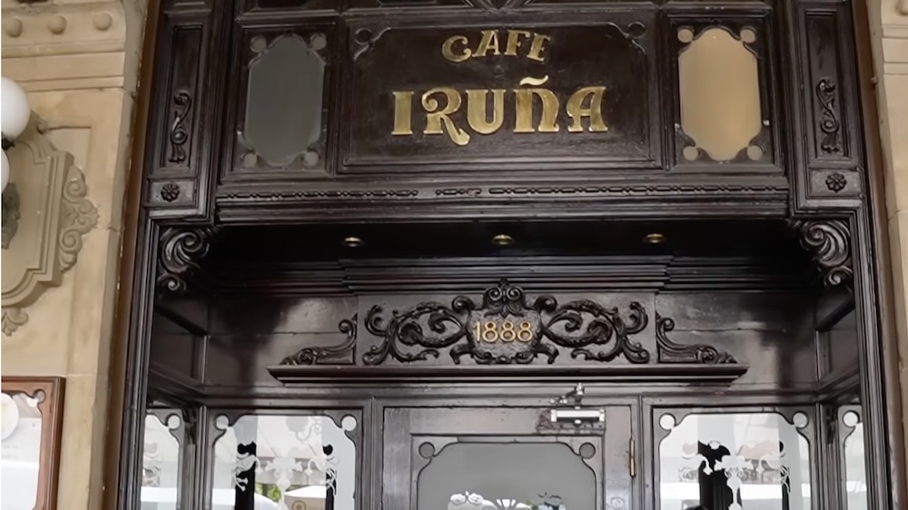 Verzierter Holzeingang zum Café Iruña mit goldener Beschriftung und der Jahreszahl 1888 über dem Eingang.