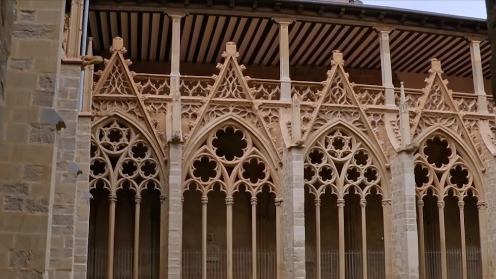 Steinbögen im gotischen Stil mit aufwendigem Maßwerk bilden die obere Fassade eines historischen Gebäudes, das sich durch Spitzbögen und dekorative Details auszeichnet.