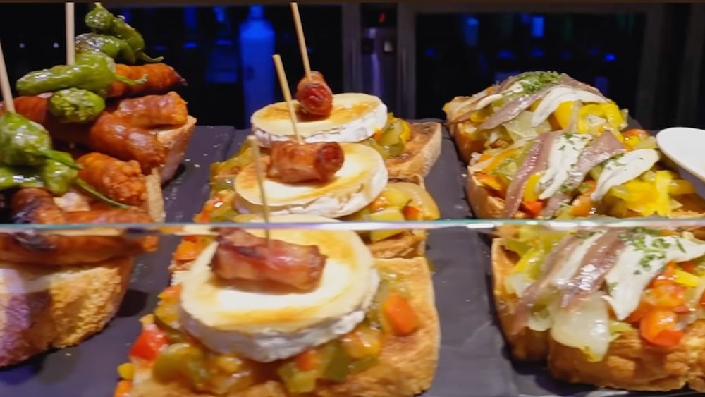 Eine Auswahl verschiedener Pintxos, darunter mit Käse, Gemüse und Sardellen belegtes Brot sowie Paprikaspieße, angerichtet auf einem Tablett.