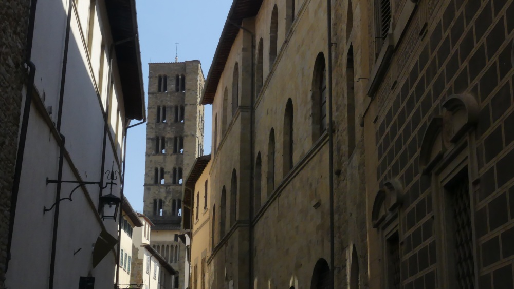 Durch eine Gasse sieht man den quadratischen Kirchturm mit vielen Fenstern.
