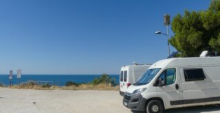 Wohnmobiltour Italien: Zwei Campervan stehen auf einem Parkplatz am Meer.